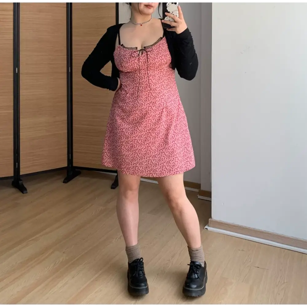 Three-quarter indoor mirror shot of pink micro floral slip mini dress, layered black cropped cardigan, one hand resting on hip, paired with chunky black leather loafers