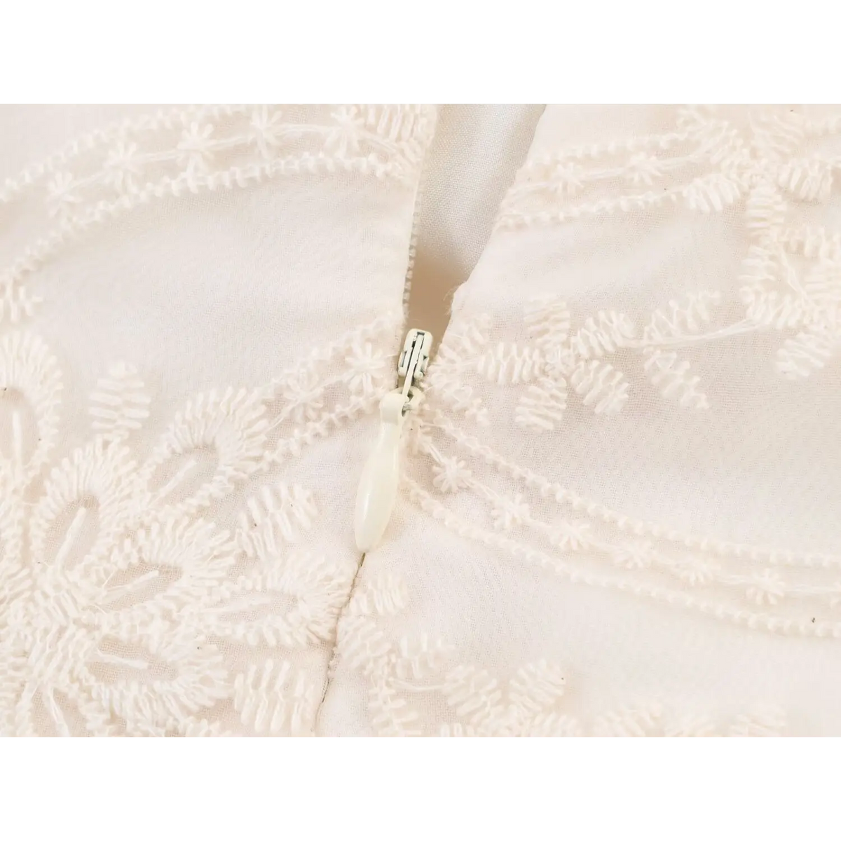 Macro close-up of invisible back zipper on beige floral embroidered mini dress, surrounded by floral lace embroidery