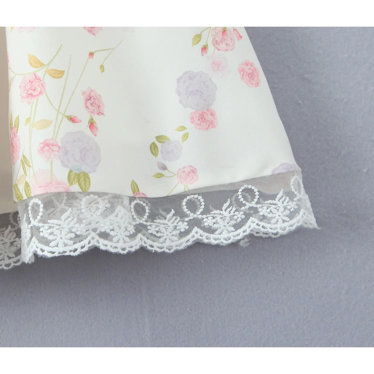 Macro detail of white scalloped lace hem trim on cream floral mini dress