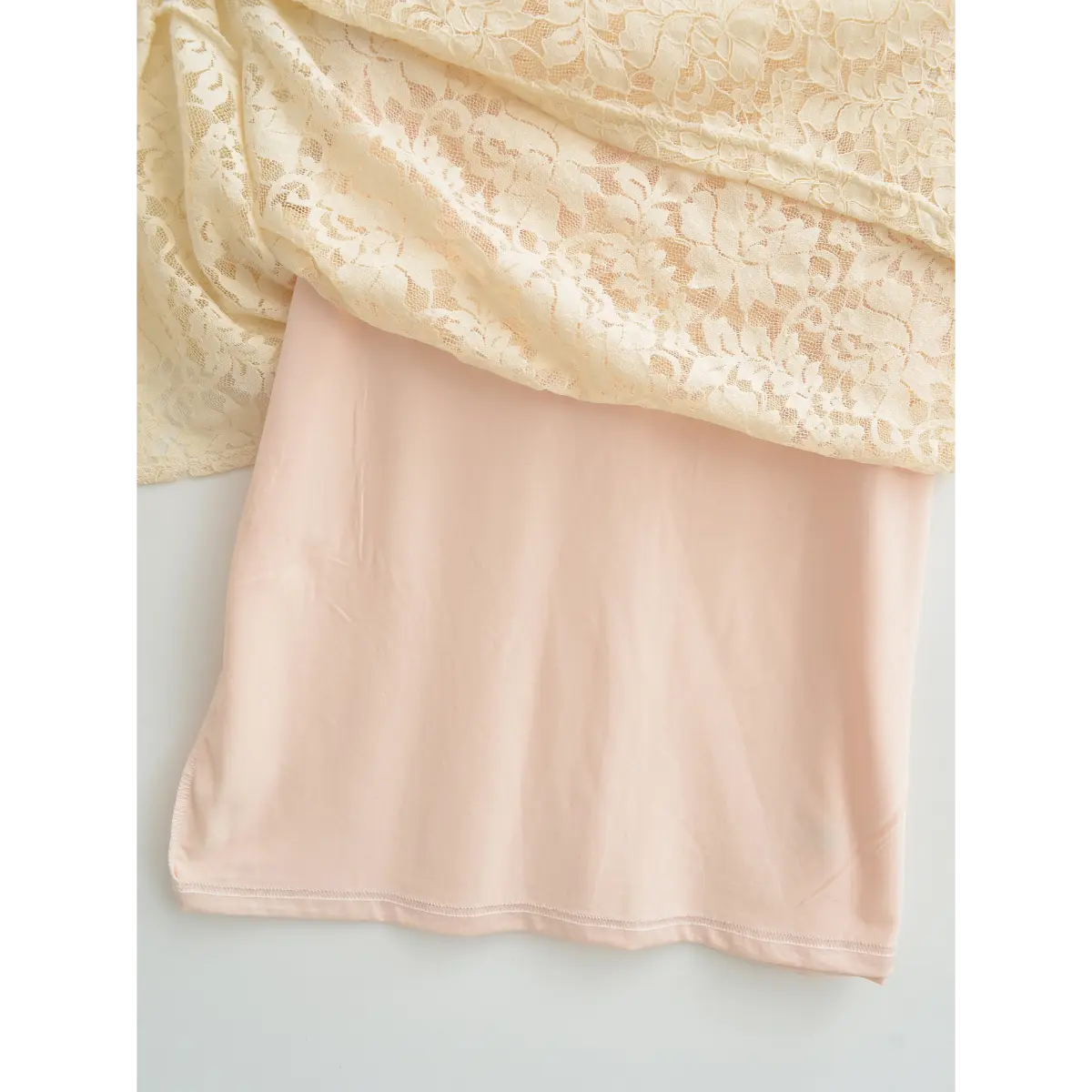 Flat lay showing cream lace overlay above soft pink inner lining
