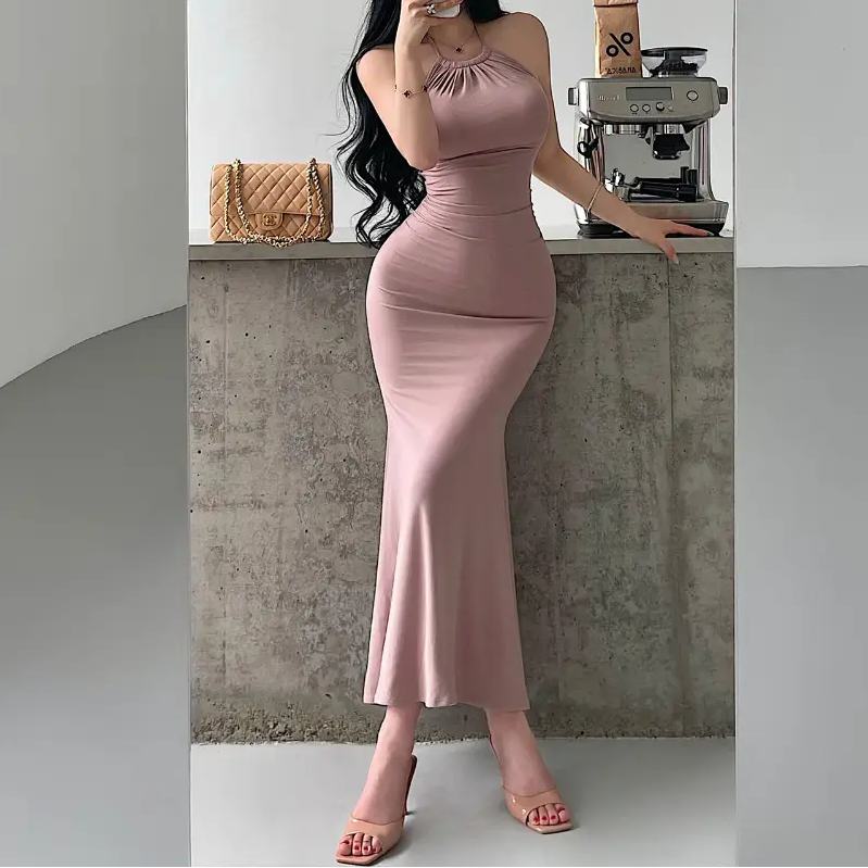 A woman wearing a dusty pink halter-neck mermaid maxi dress with ruched waist and bodycon fit, styled with nude accessories.