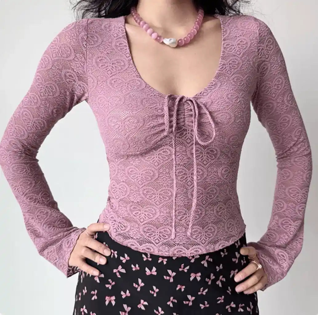 Model wearing dusty pink lace long sleeve tie‑front crop top, hands on hip pose