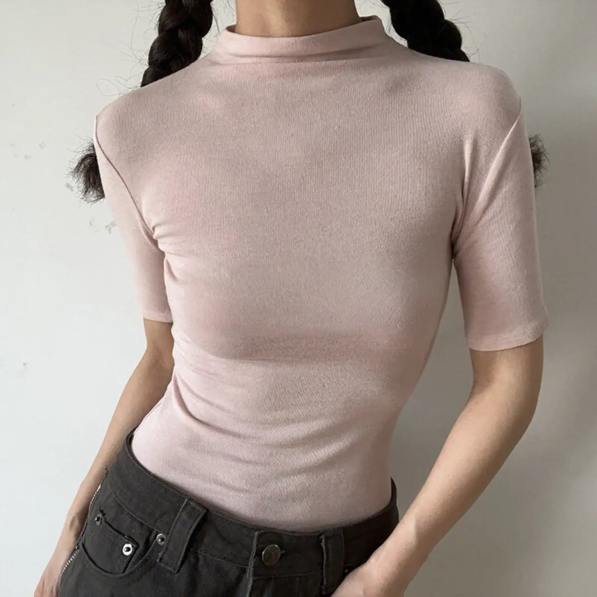Lifestyle shot of form-fitting dusty pink ribbed half-turtleneck short-sleeve top, tucked into jeans