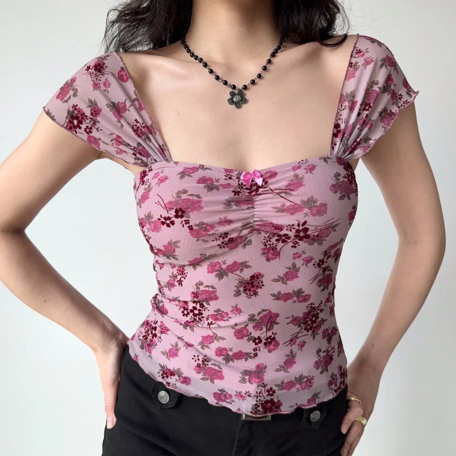 Front lifestyle shot on model of dusty pink rose printed mesh top, square neck, front ruched detail, tiny pink bow, flutter cap sleeves