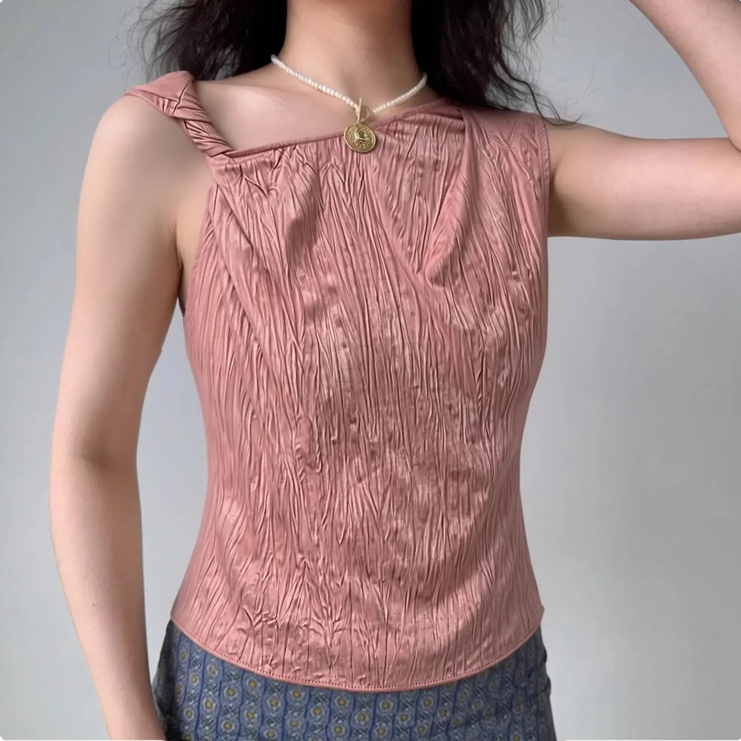 Lifestyle wearing shot of dusty rose crinkled satin twist shoulder sleeveless top, paired with patterned bottoms