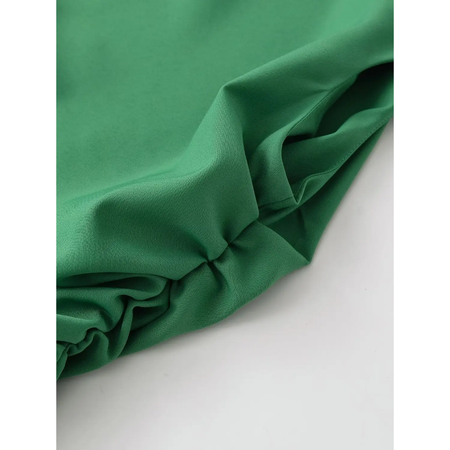 Macro close-up of smooth emerald green crepe fabric texture with natural drape and ruched fold detail