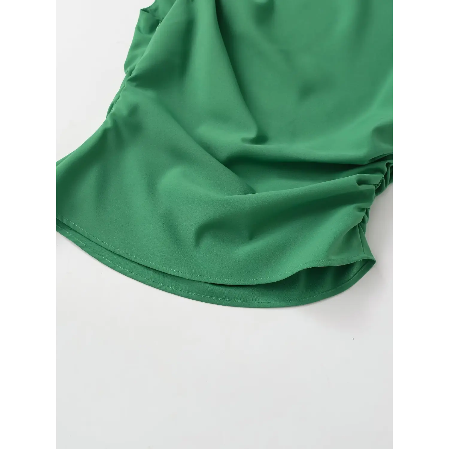 Close-up of side gathered ruched detail on emerald green crepe top bottom hem
