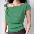 Lifestyle wearing shot of emerald green one-shoulder crepe top with twisted neckline and side ruched detail, paired with dark bottoms