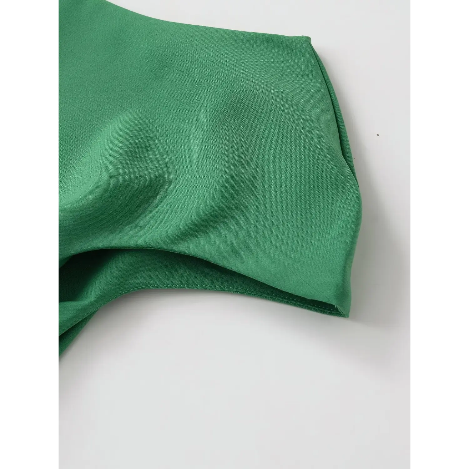 Close-up of twisted one-shoulder neckline detail on emerald green crepe top