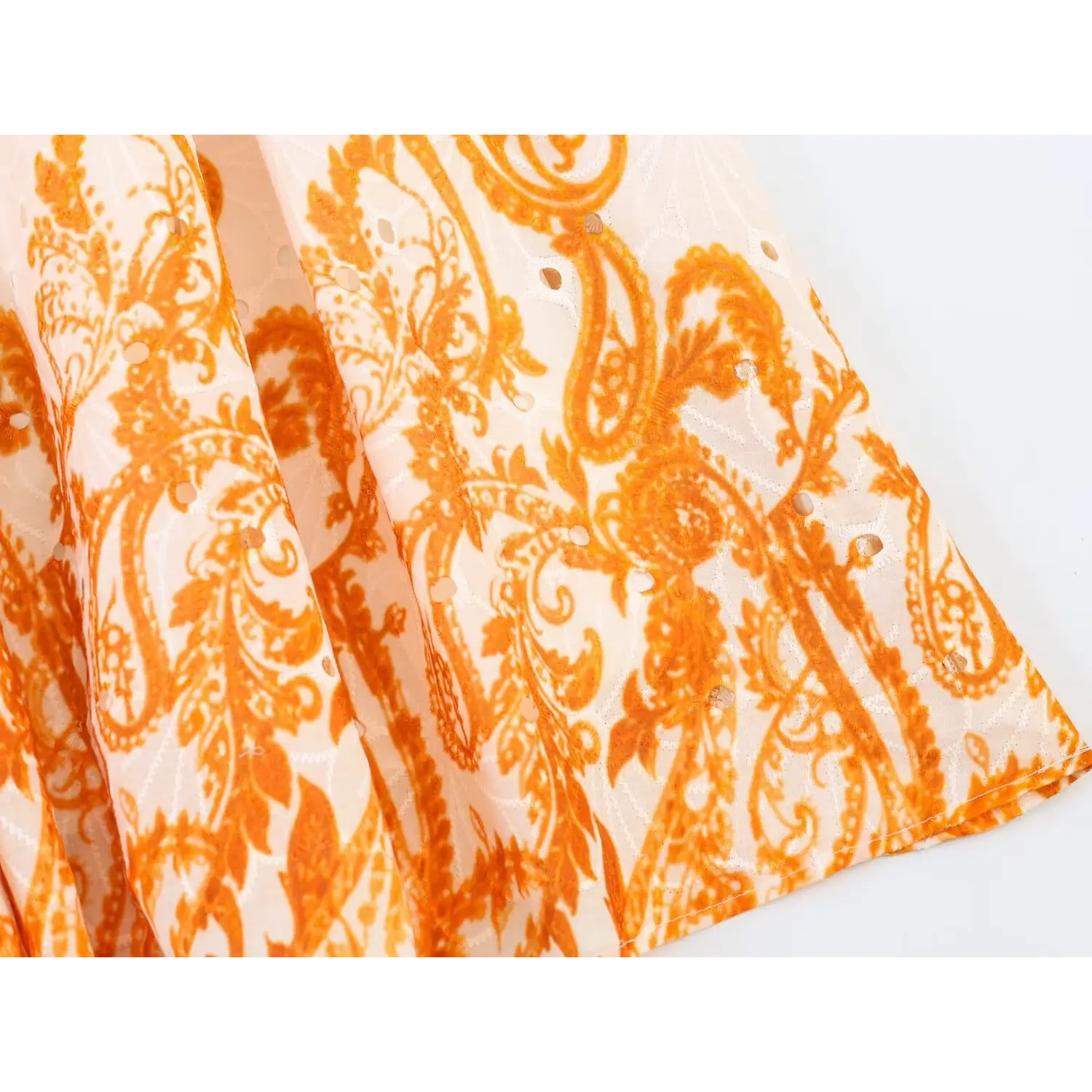 Macro texture shot of eyelet cutwork overlay with orange paisley vintage printing