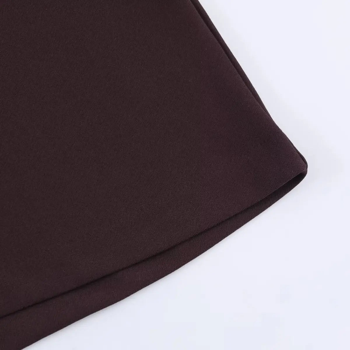 Close-up of the fabric texture and folded hem on a brown V-neck cap sleeve dress, showing the smooth, matte finish.
