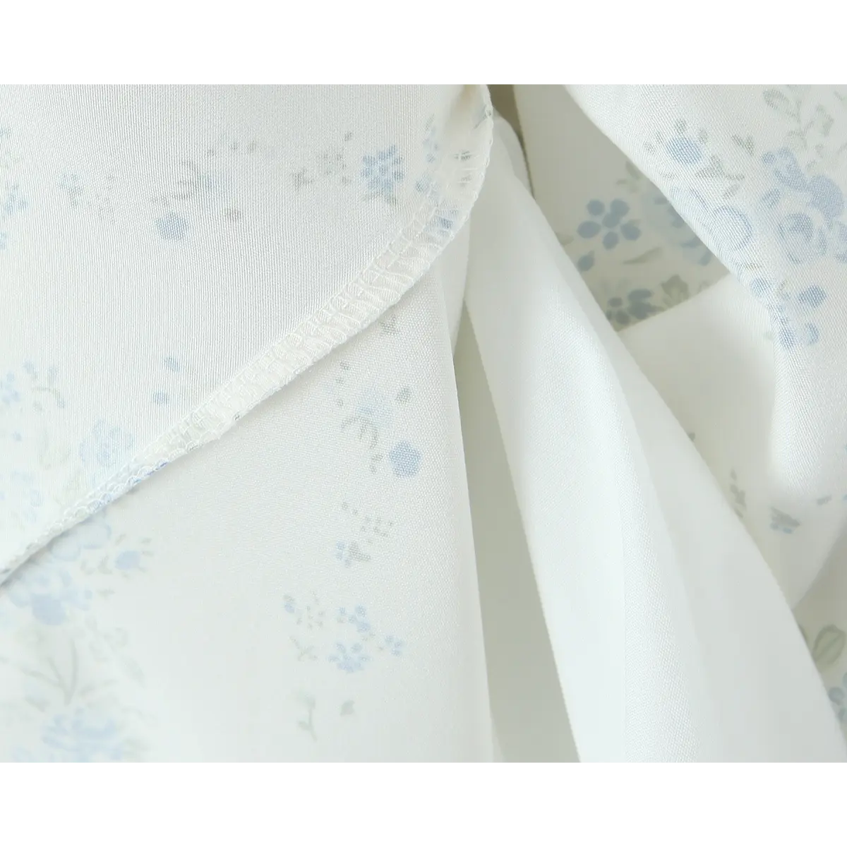 Close-up of the fabric and stitched seam on a cream floral dress, showing the blue floral print and clean finish.