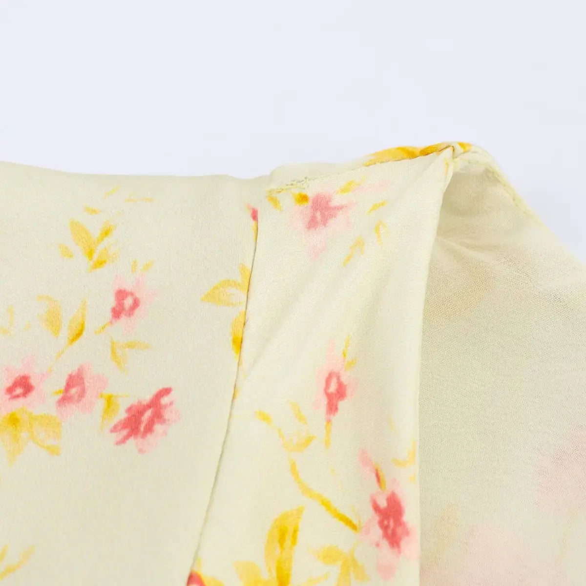 Close-up of the fabric and side seam on a pale yellow floral dress, showing the lining and construction.