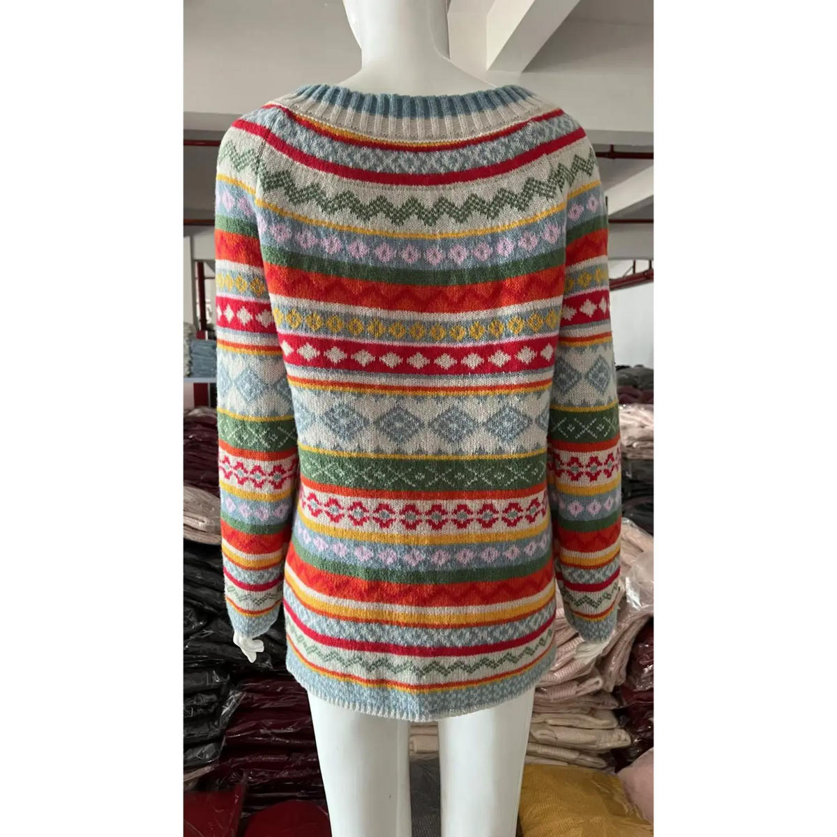 White mannequin back view showing fair isle jacquard knit sweater, multicolor geometric stripe pattern, boat neckline, factory warehouse background