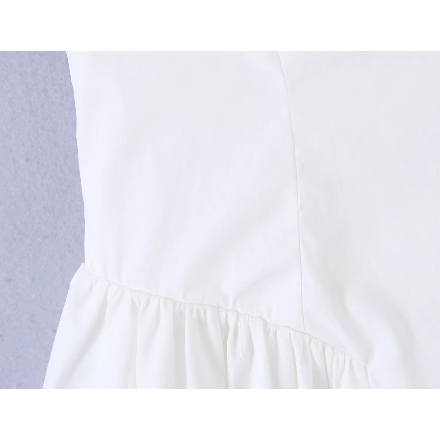 Close-up of seamed fitted waist and skirt gathering on white cami mini dress