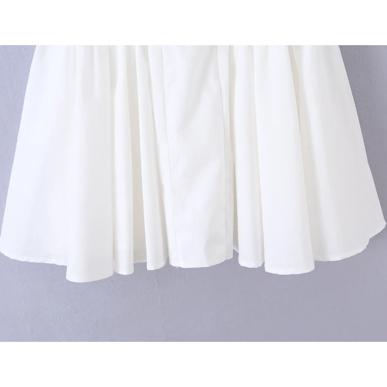 Gathered flare skirt hem close-up, flowy A-line bottom of white spaghetti strap dress