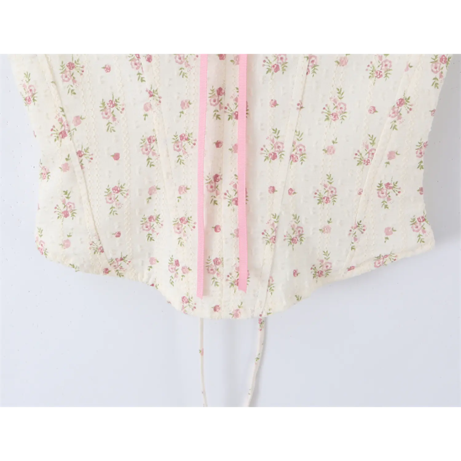 Close-up of the front hem and pink ribbon tie on the floral print corset-style camisole top
