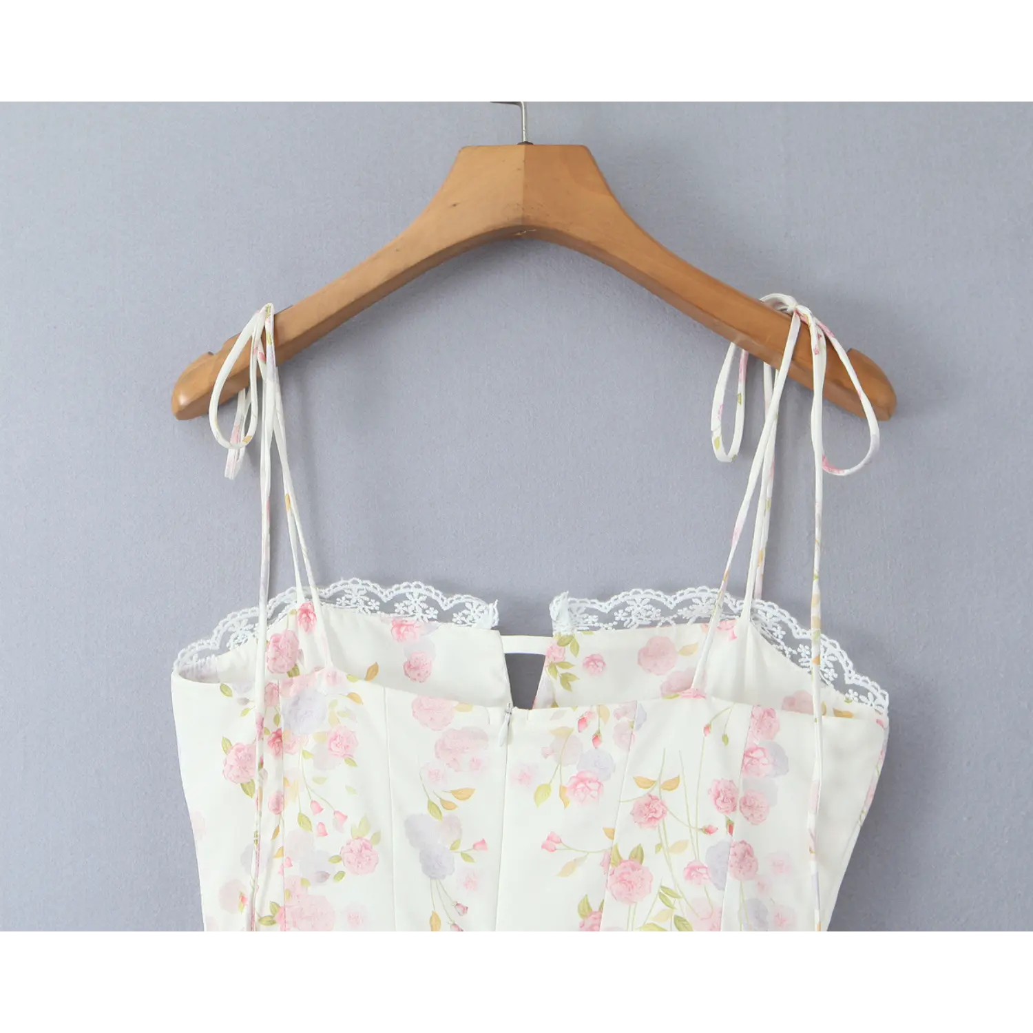 Back partial shot, cream floral corset cami dress with tie spaghetti straps hanging on wooden hanger