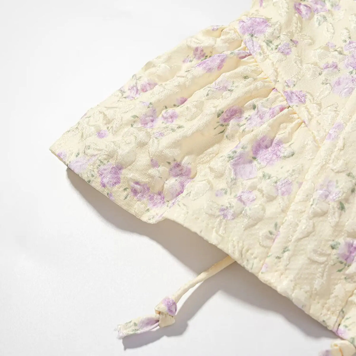 Close-up shot of peplum ruffle hem and fabric tie end of pale yellow purple floral corset cami top