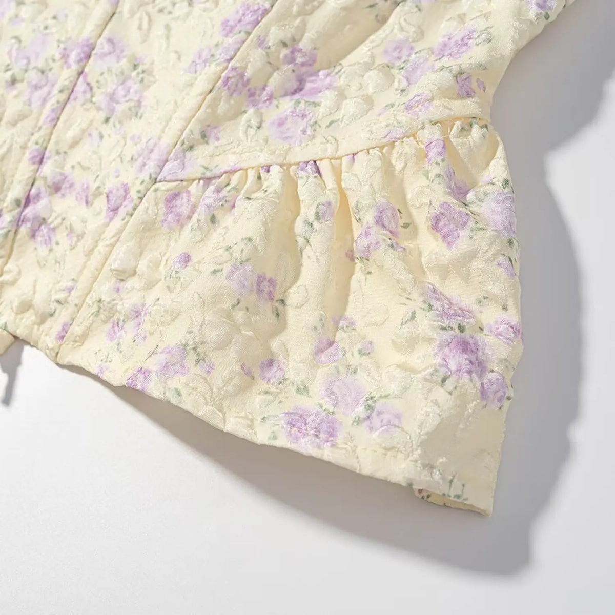 Macro detail of textured jacquard fabric and peplum ruffle hem on pale yellow purple floral corset cami top