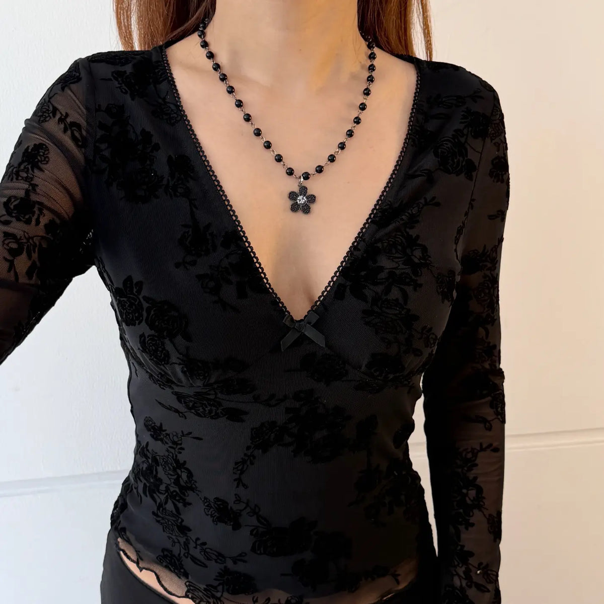 Model wearing floral flocked v neck bow mesh long sleeve top, indoor close-up view