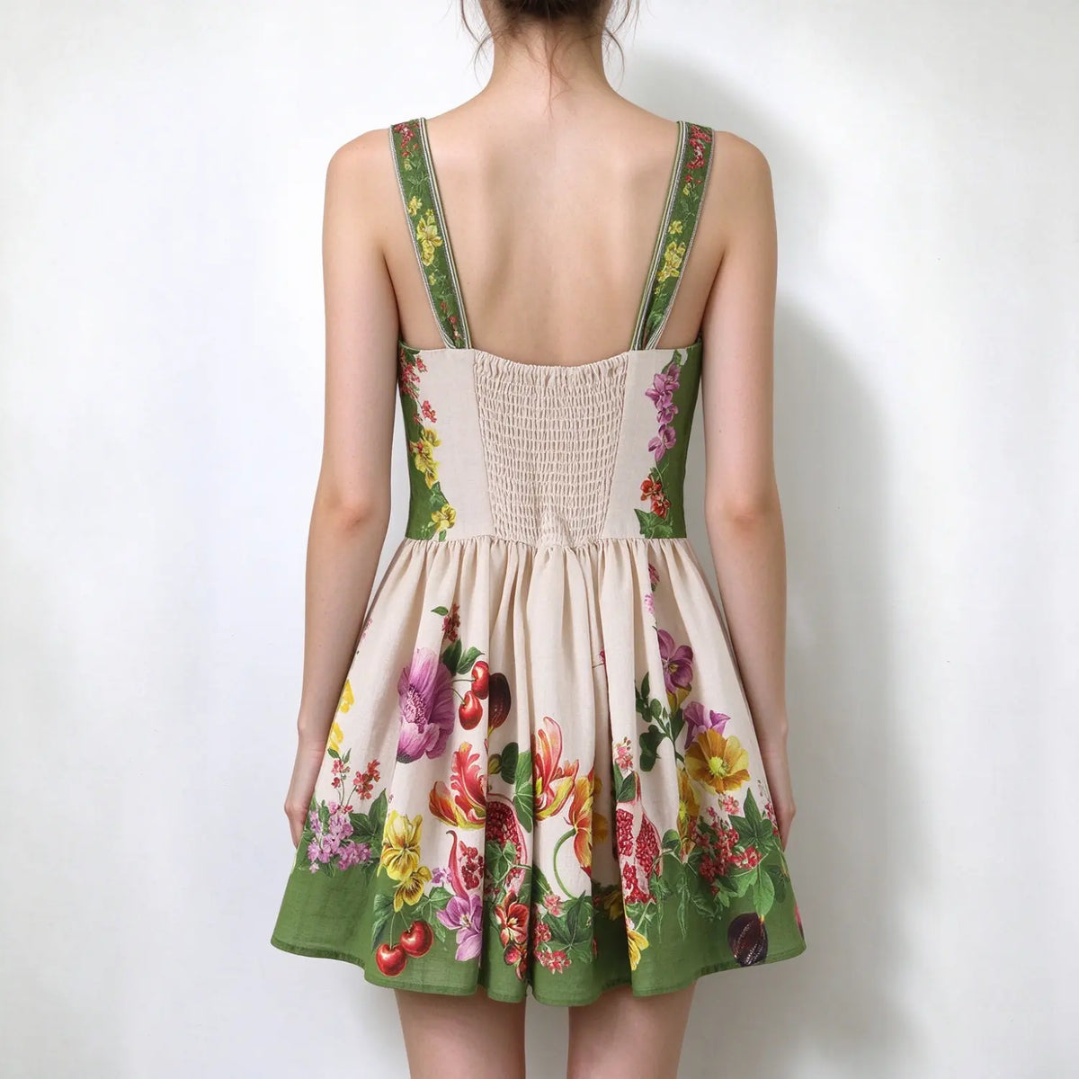 Model back view, floral fruit print spaghetti strap mini dress, smocked elastic back panel, wide printed shoulder straps, flared skater skirt with green hem