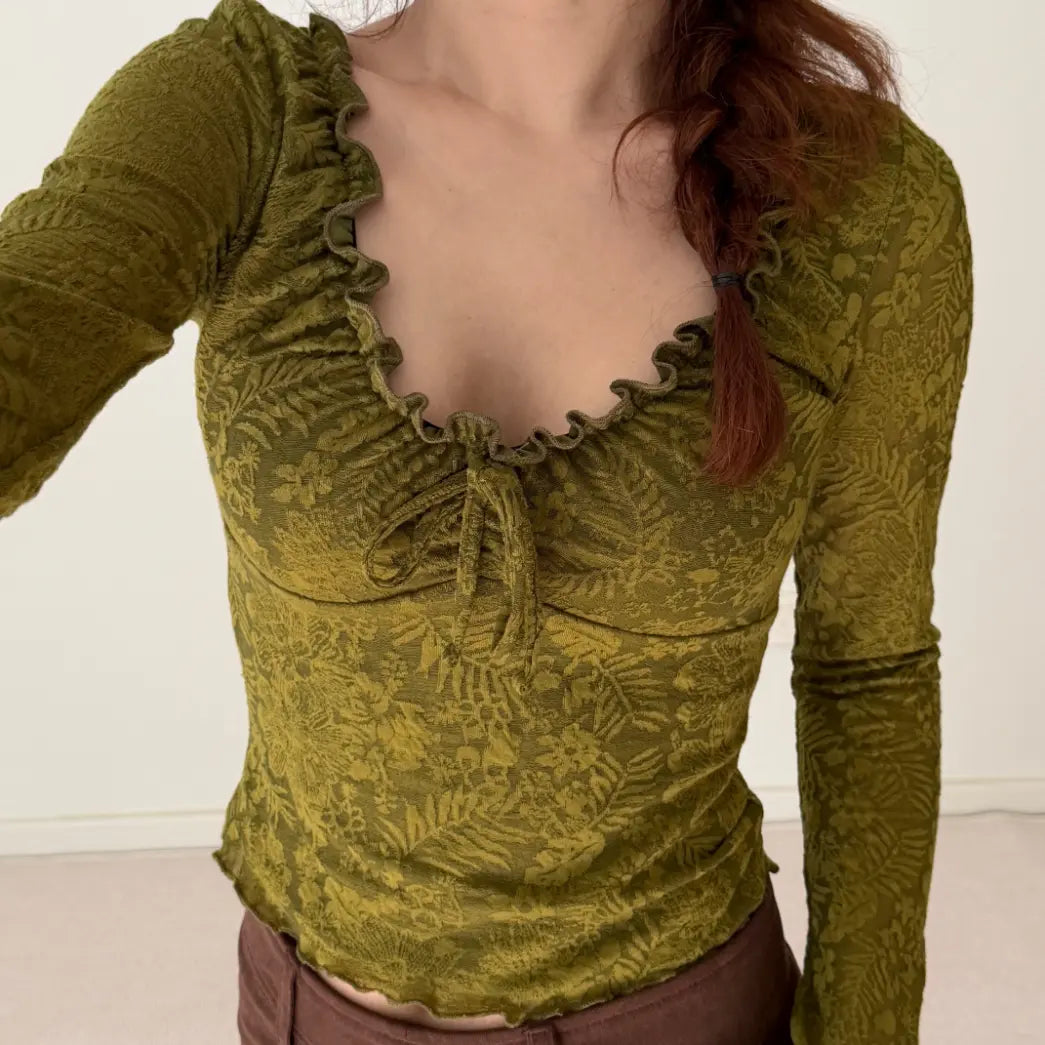 Model wearing olive floral jacquard ruffle tie neck bell sleeve crop top, indoor close-up view