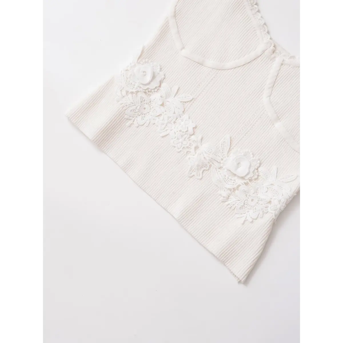 Close-up of the 3D floral lace appliqu on the waist of a white ribbed cami top.