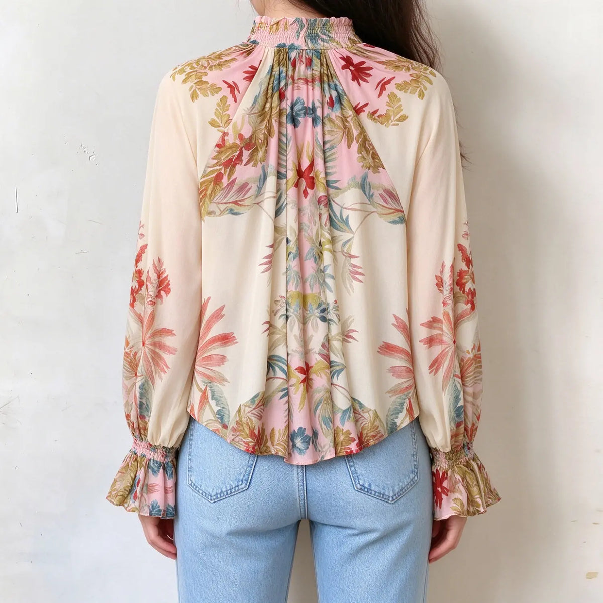 Female model in cream floral printed blouse, back view showing gathered smocked ruffle neck, loose flowy back silhouette and full printed sleeves
