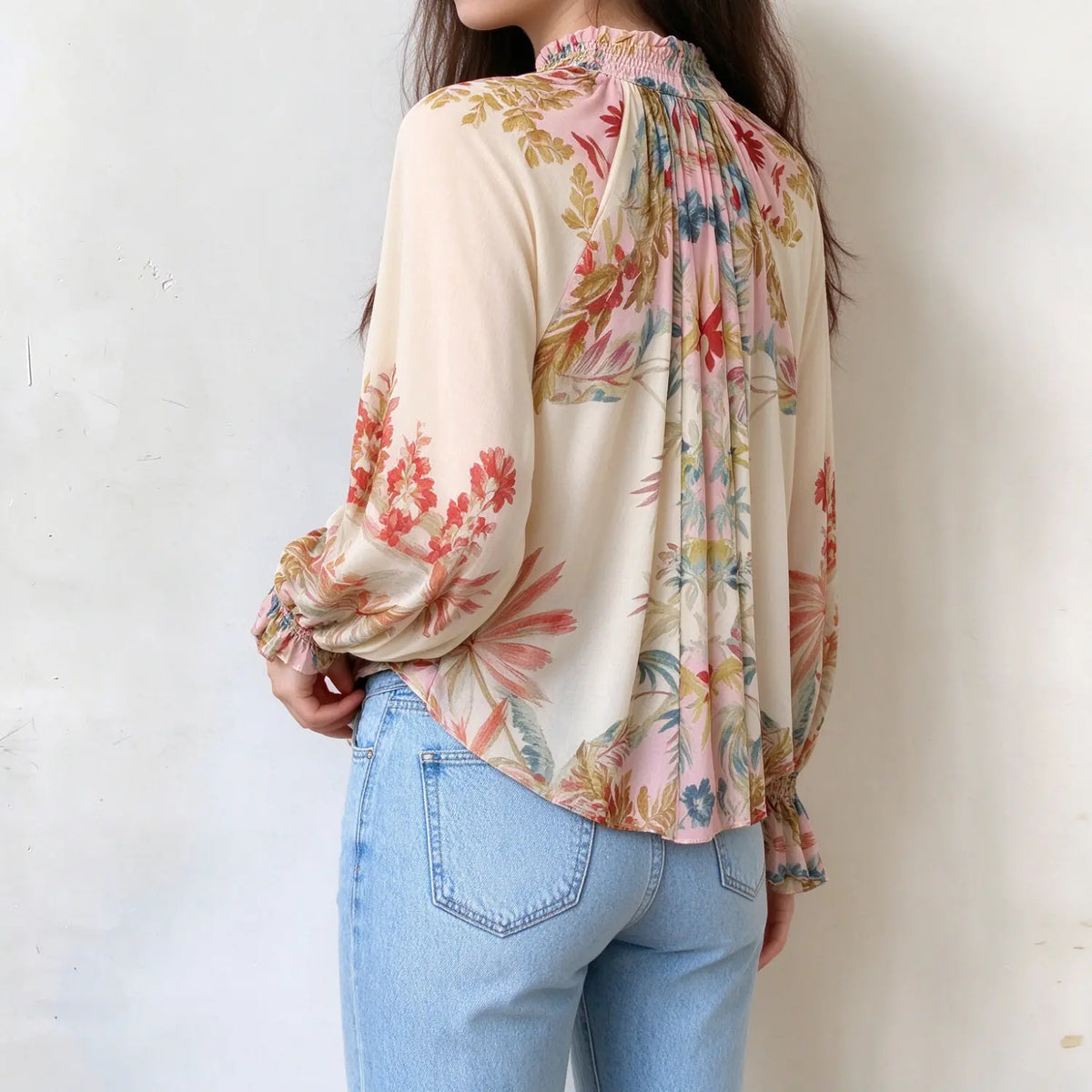 Female model wearing floral print ruffle neck blouse, side back angle, show fabric drape and full floral pattern on sleeves and hem