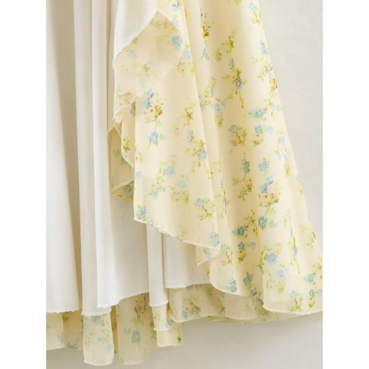 Close-up of the ruffled skirt fabric of floral maxi dress, pale yellow base with blue small floral print, flowy chiffon material