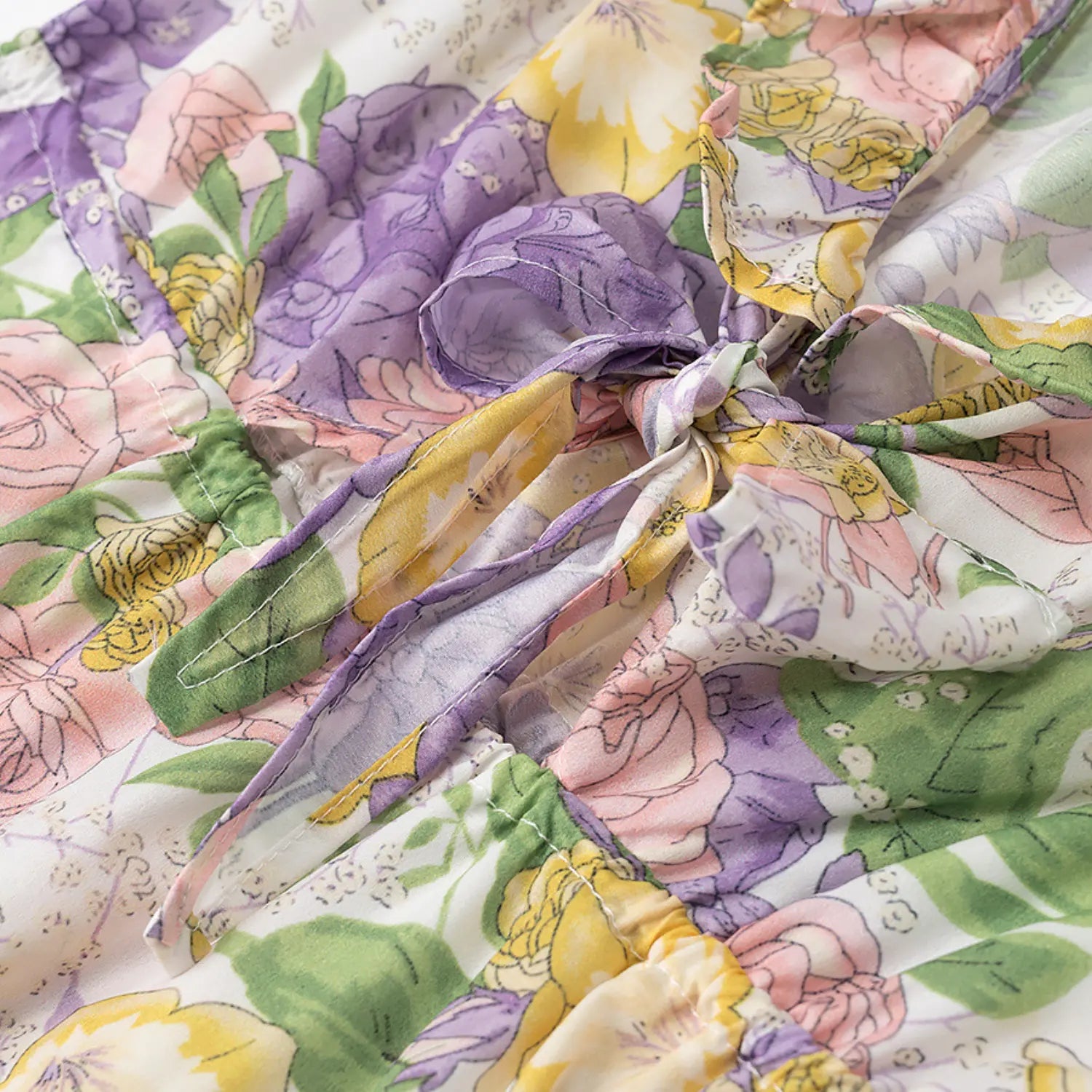 Close-up of adjustable front fabric tie knot at waist on purple pink yellow floral print dress