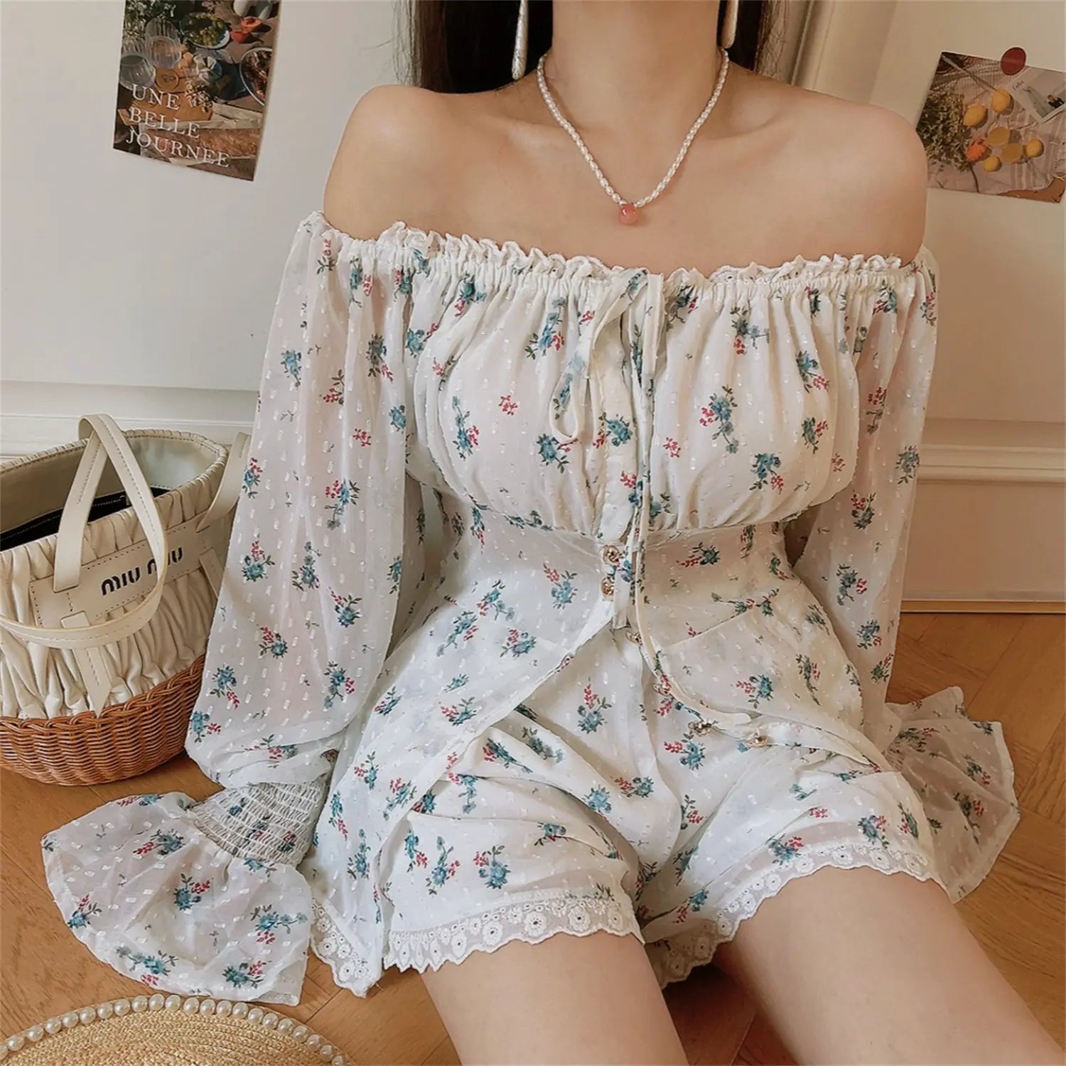 Relax spread leg sitting lifestyle shot white blue flower two piece outfit, off shoulder bubble long sleeve, full front button down top, high waist matching floral shorts with lace trim