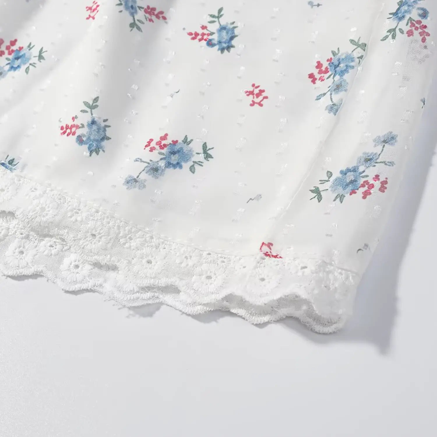 Closeup of matching floral shorts bottom scalloped eyelet lace trim hem, white swiss dot tiny blue flower fabric, neat overlock stitching, lightweight sheer woven texture