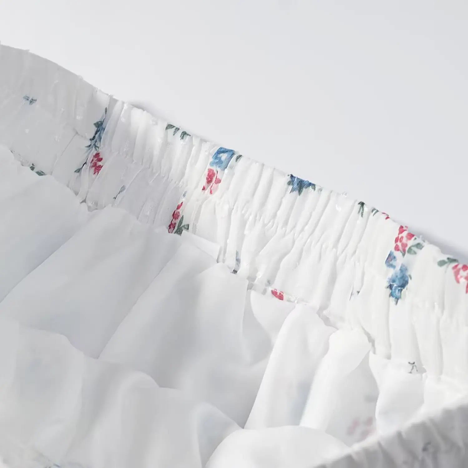 Extreme closeup shorts waist elastic shirring stitching, neat folded binding seam, uniform tiny floral print on white swiss dot fabric
