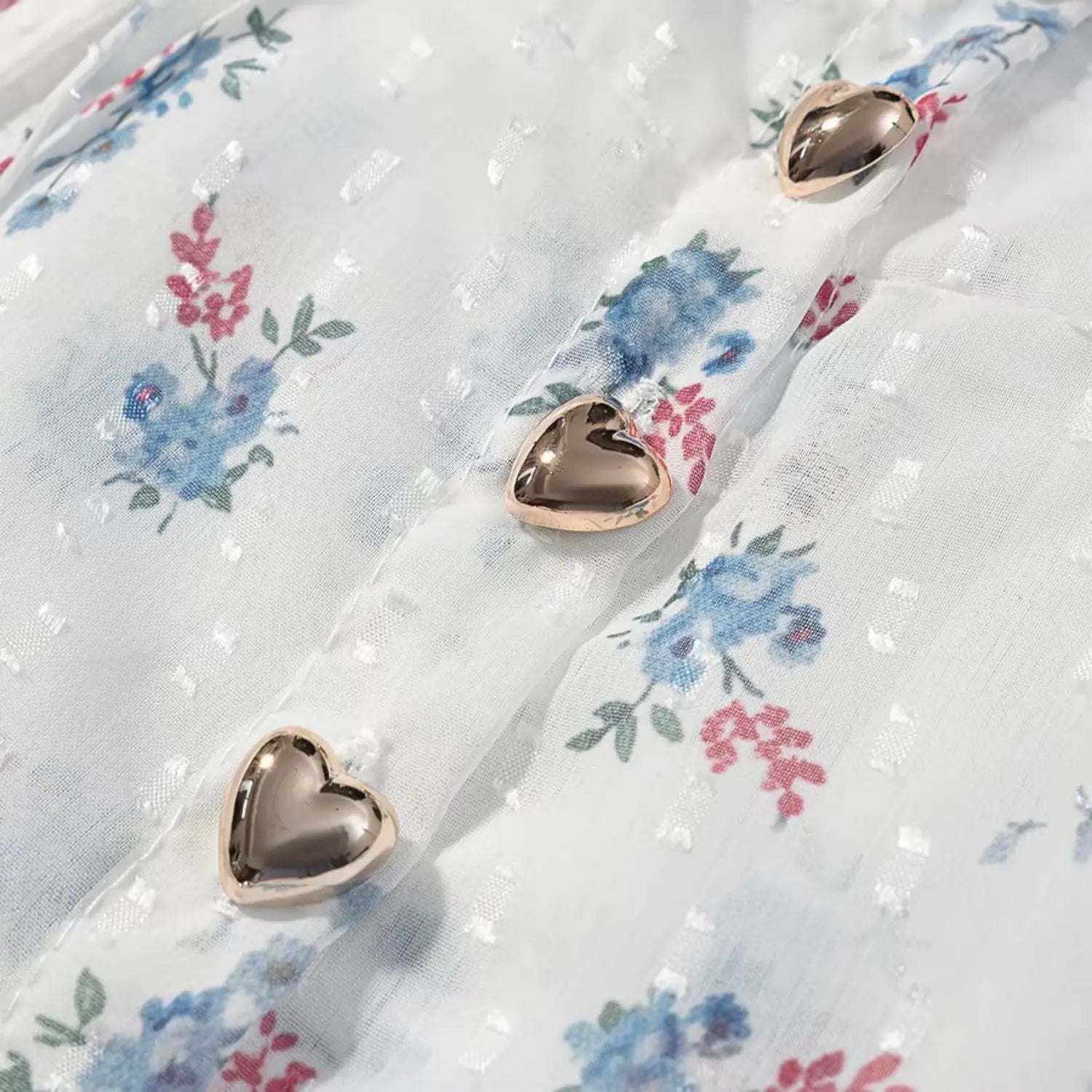 Extreme closeup vertical front placket, rose gold heart shaped metal buttons, neat topstitch seam, blue floral swiss dot fabric