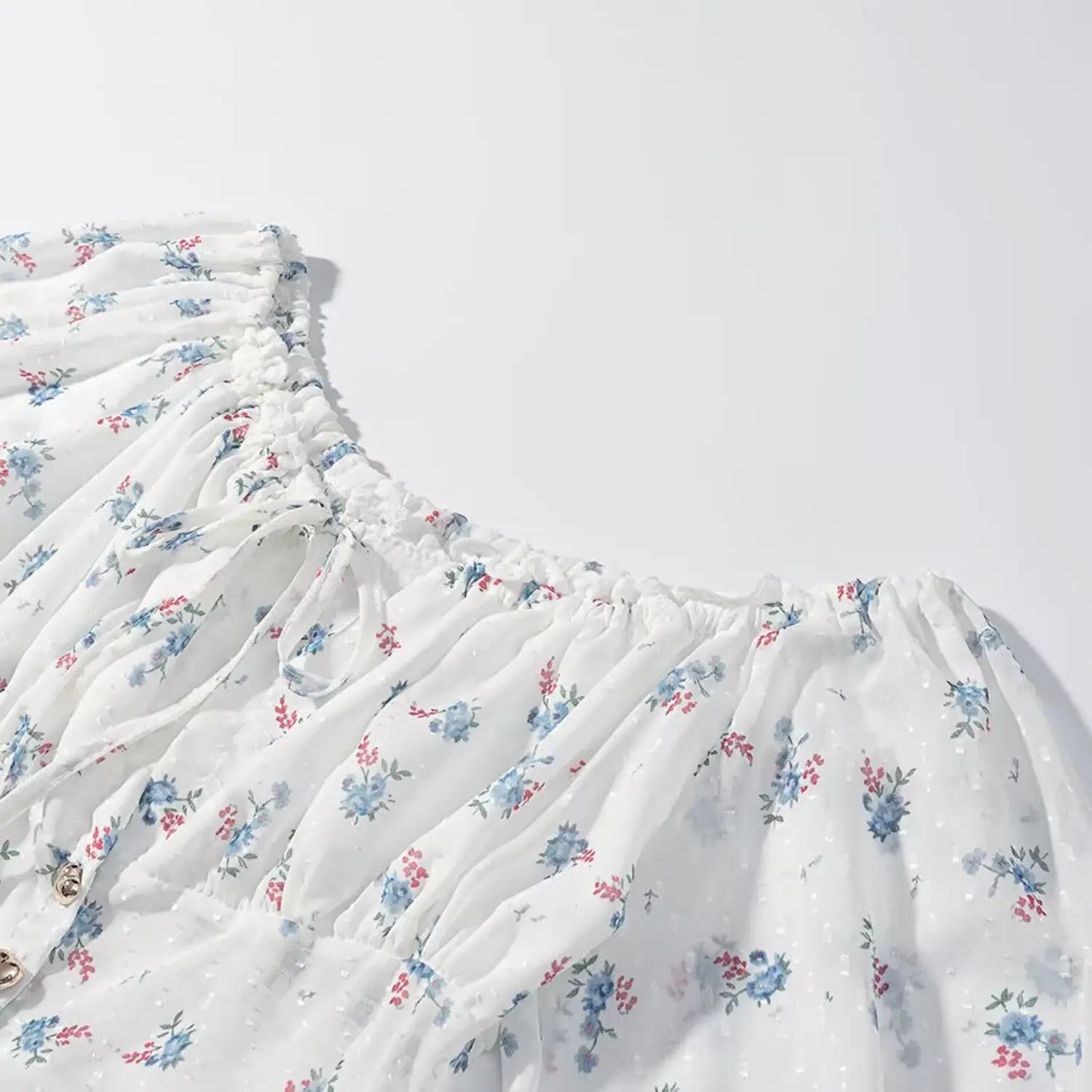 Closeup off shoulder elastic ruffle neckband, bust self-fabric drawstring tie, white swiss dot fabric with tiny blue floral print, full horizontal shirring at neckline