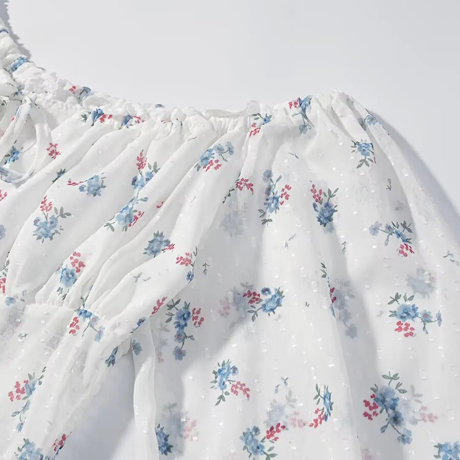 Partial shoulder & sleeve fabric macro shot, swiss dot crinkle texture, evenly distributed blue & red mini floral print, lightweight sheer woven material