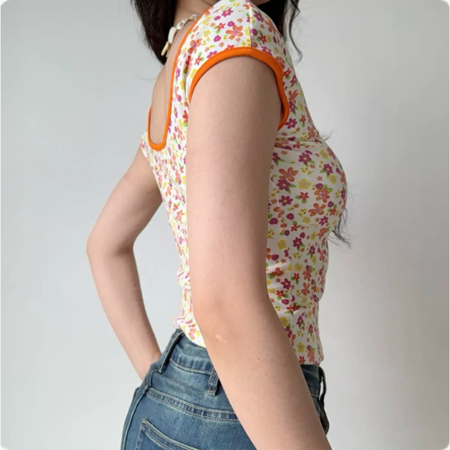 Lifestyle back shot of a woman wearing a fitted floral print top with orange trim