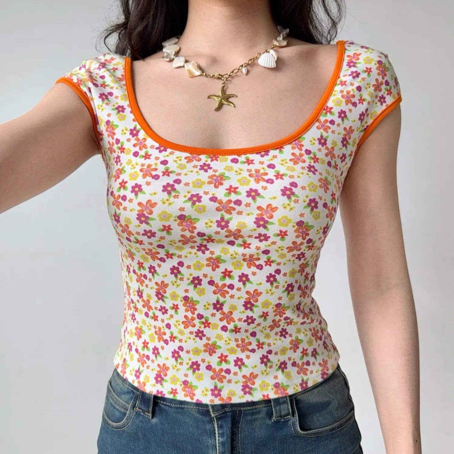 Selfie shot of a woman in a fitted floral print top with orange trim and a shell necklace