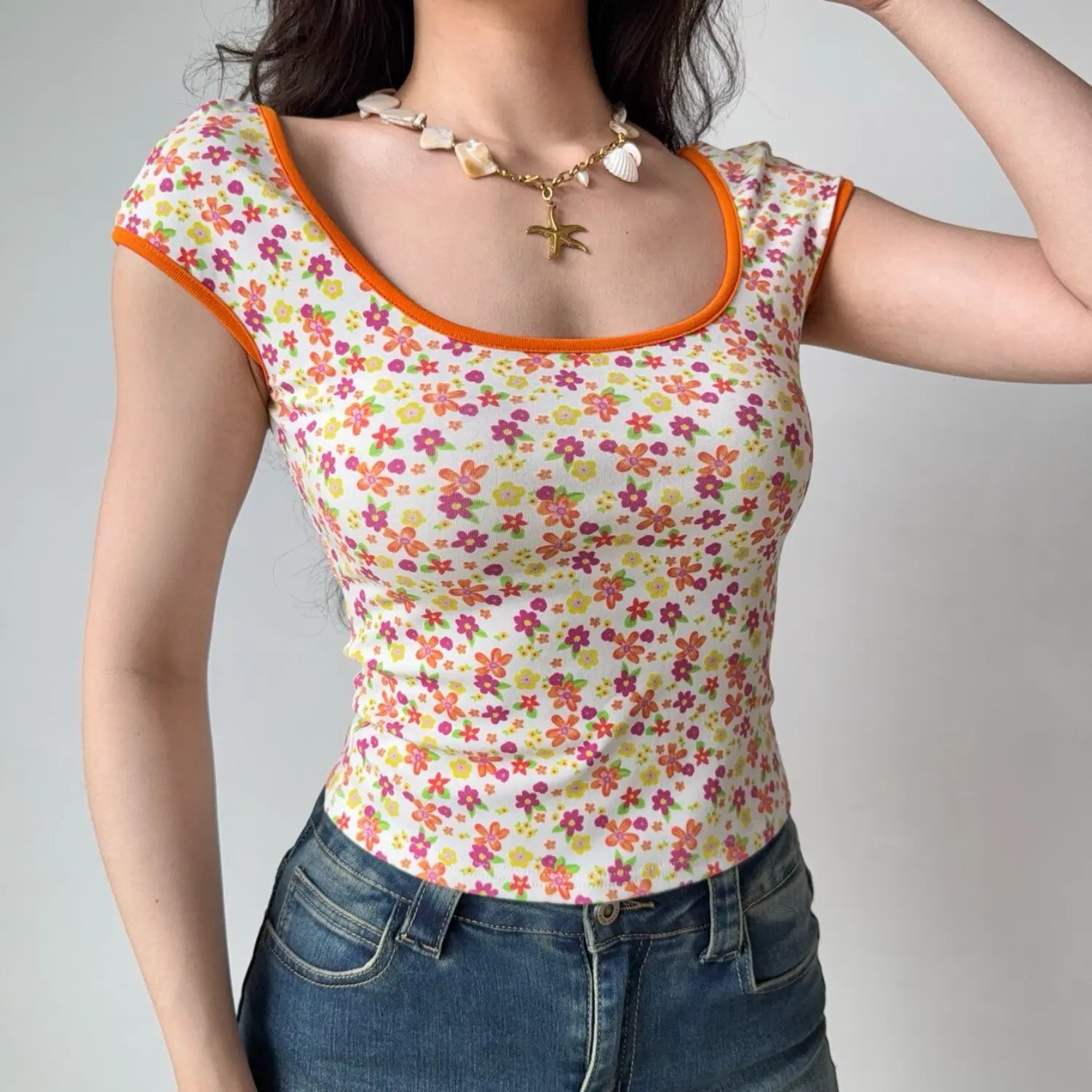 Lifestyle shot of a woman in a fitted floral print top with orange trim, raising one hand