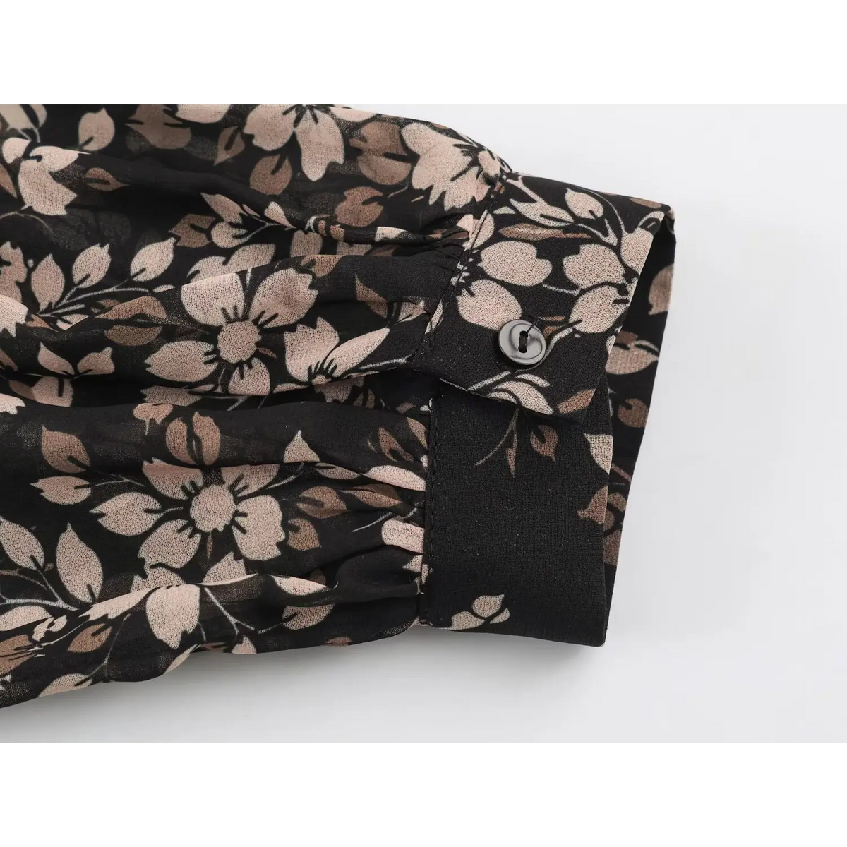 Close-up of gathered cuff with black binding and round metal button on floral print dress