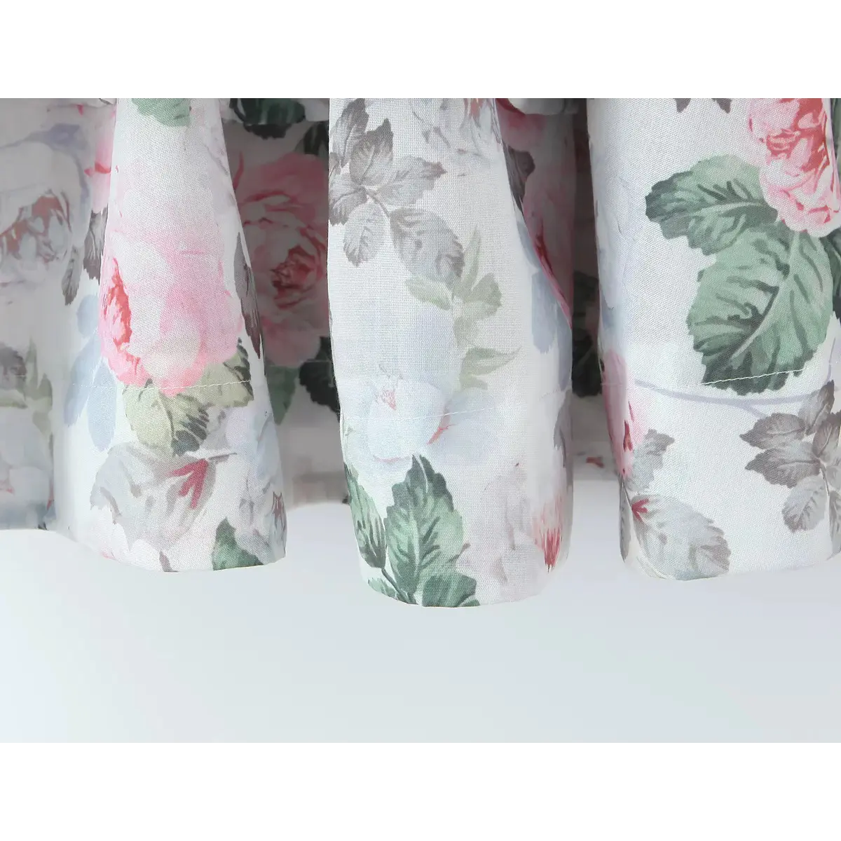 Close-up of the hem and tiered skirt of a pink rose and green leaf print dress.