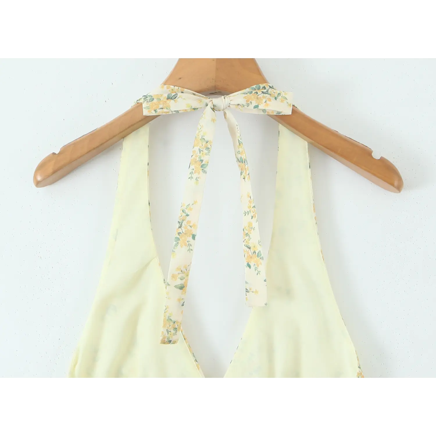 Back view close‑up of halter tie bow on wooden hanger for yellow floral print mini dress