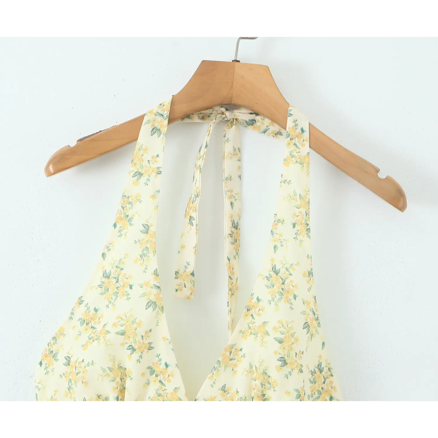 Close‑up of halter neck tie detail for yellow floral print mini dress hanging on wooden hanger