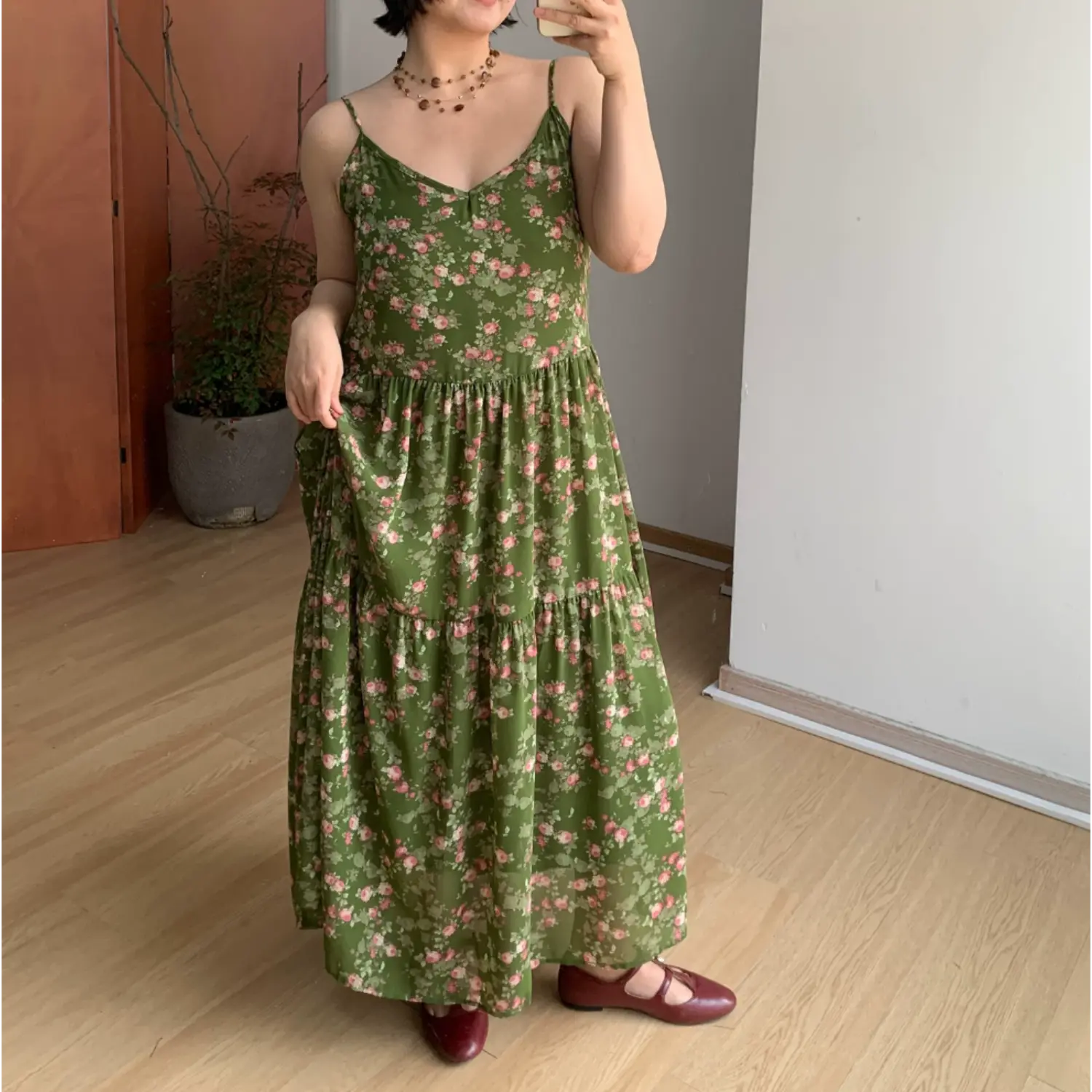 Indoor mirror full front shot of dark green tiny pink floral tier slip maxi dress, simple V-neck spaghetti straps, fitted empire waist, burgundy mary jane flat shoes
