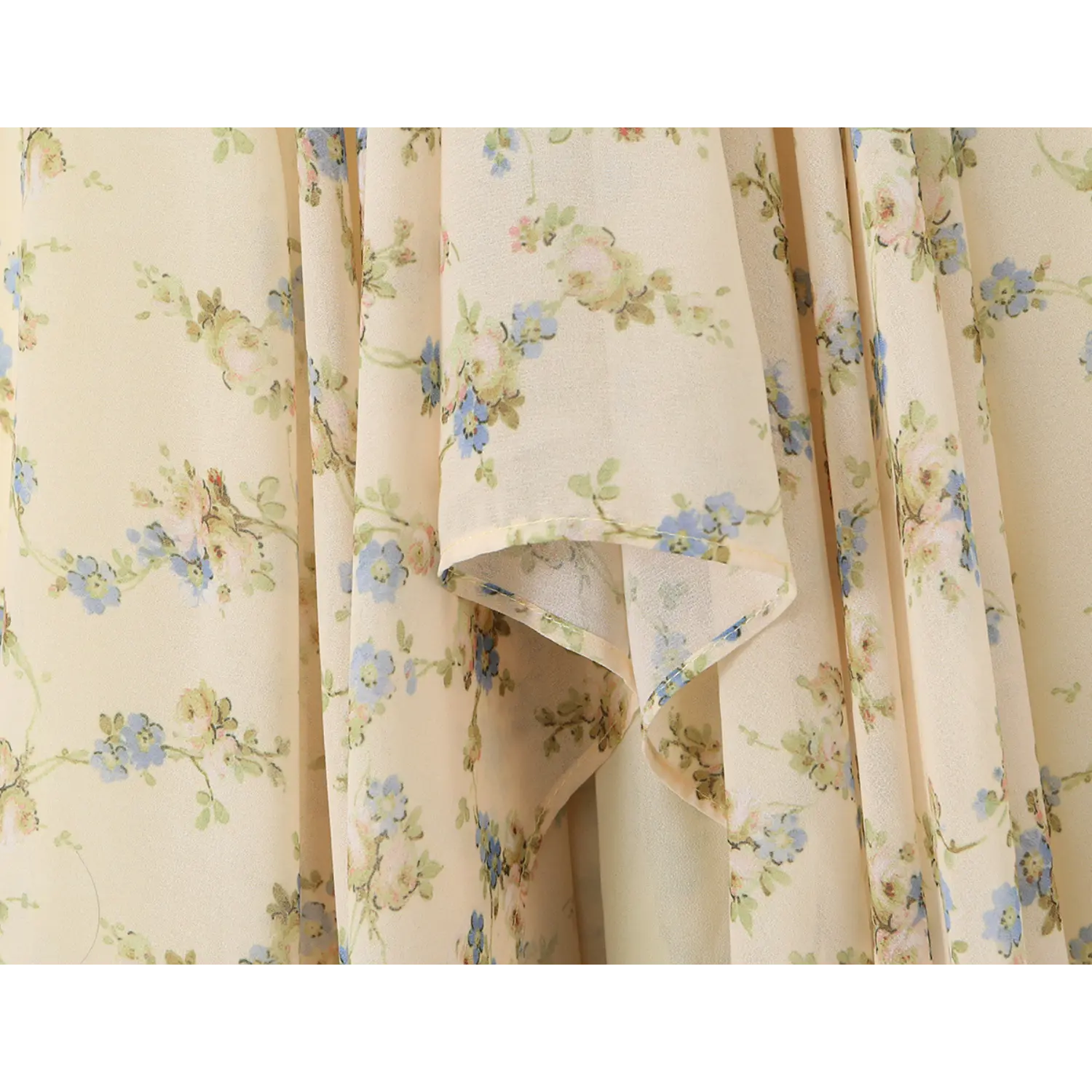 Textured close-up of sheer chiffon skirt folds, pale cream base decorated with scattered blue wildflowers and thin finished fabric hems