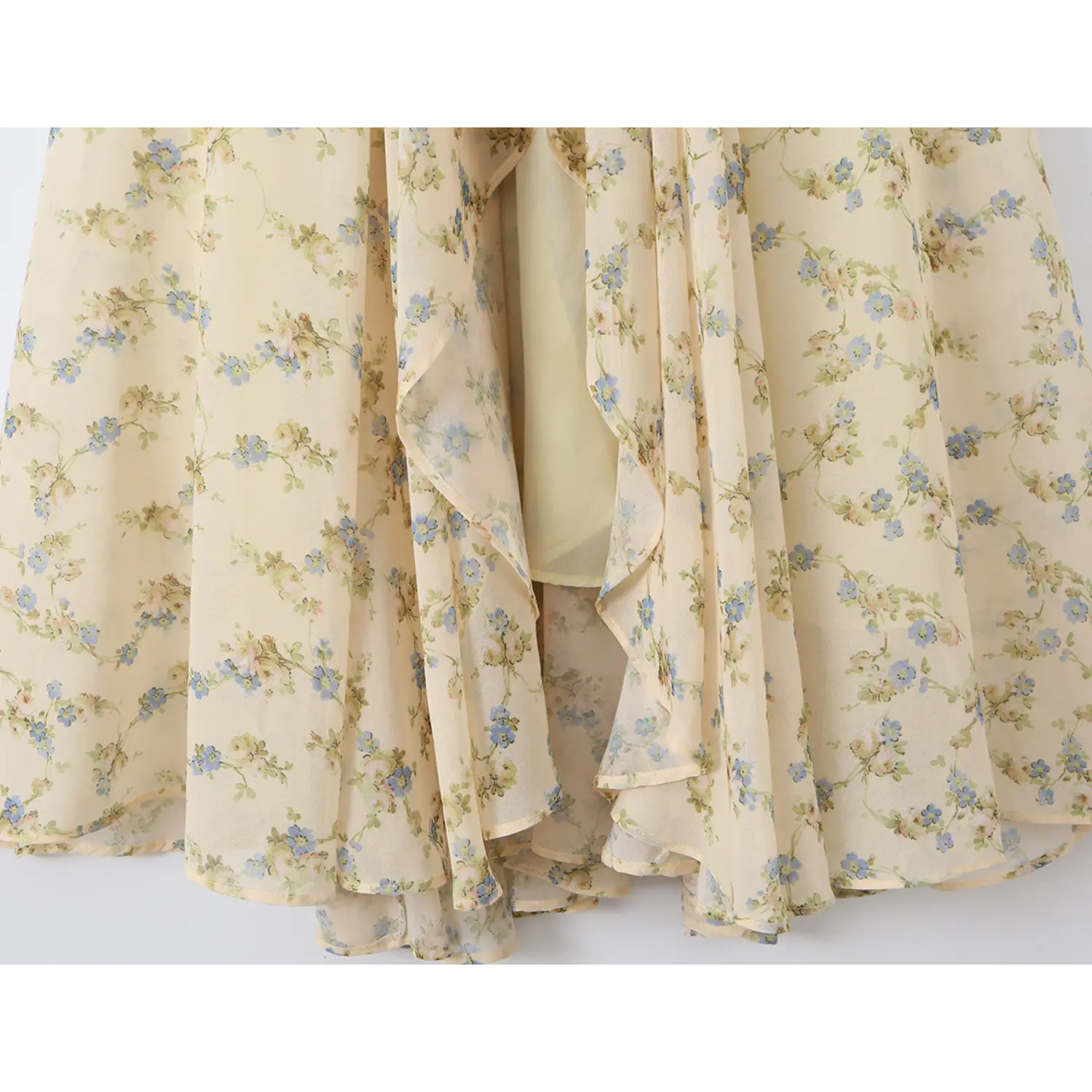 Close layered shot of ruffled mermaid skirt hem, flowy sheer cream chiffon scattered with blue and pink tiny flowers with matching inner lining