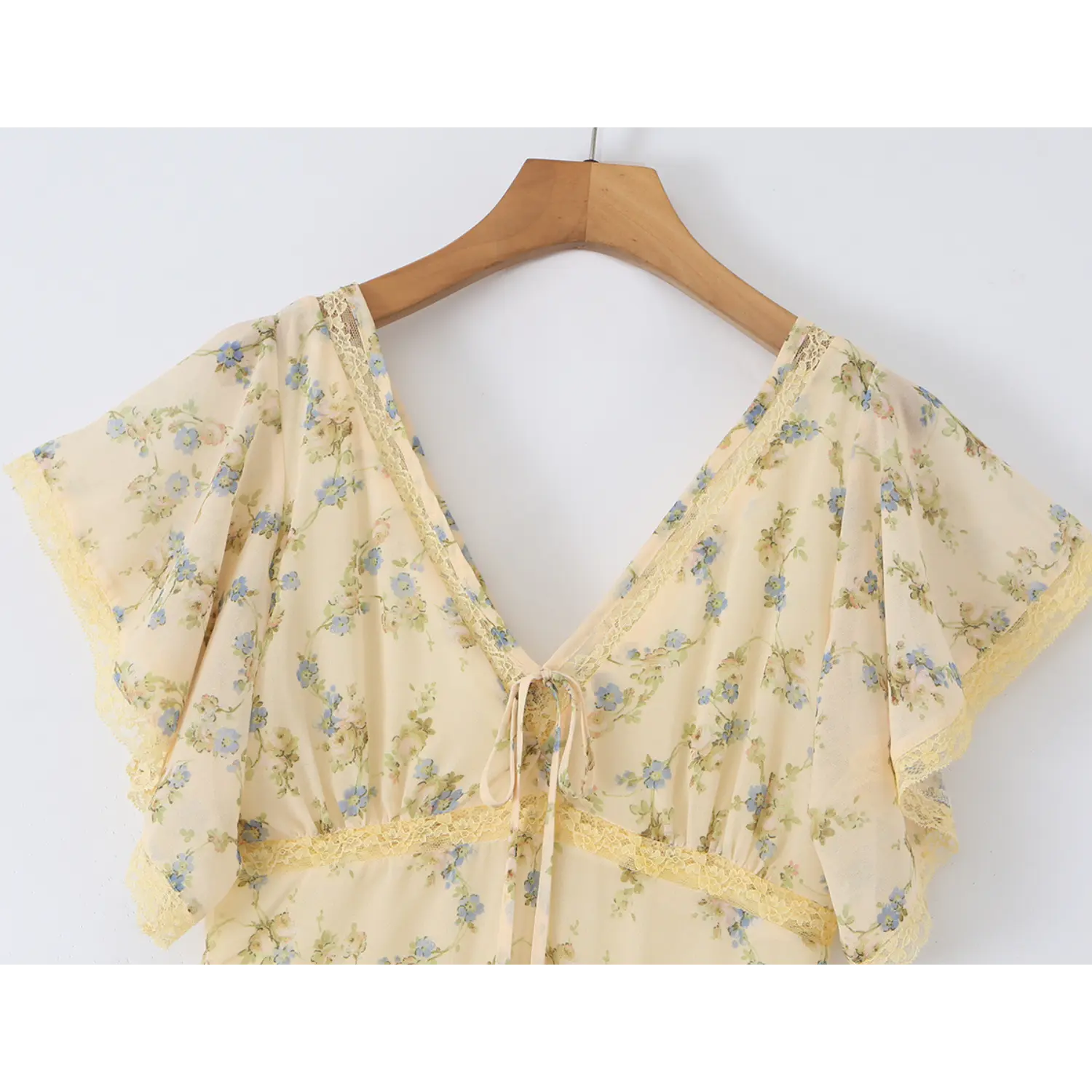 Hanging medium close shot of v-neck bust with fabric tie and yellow lace trim, semi-sheer cream chiffon scattered with small blue wildflowers