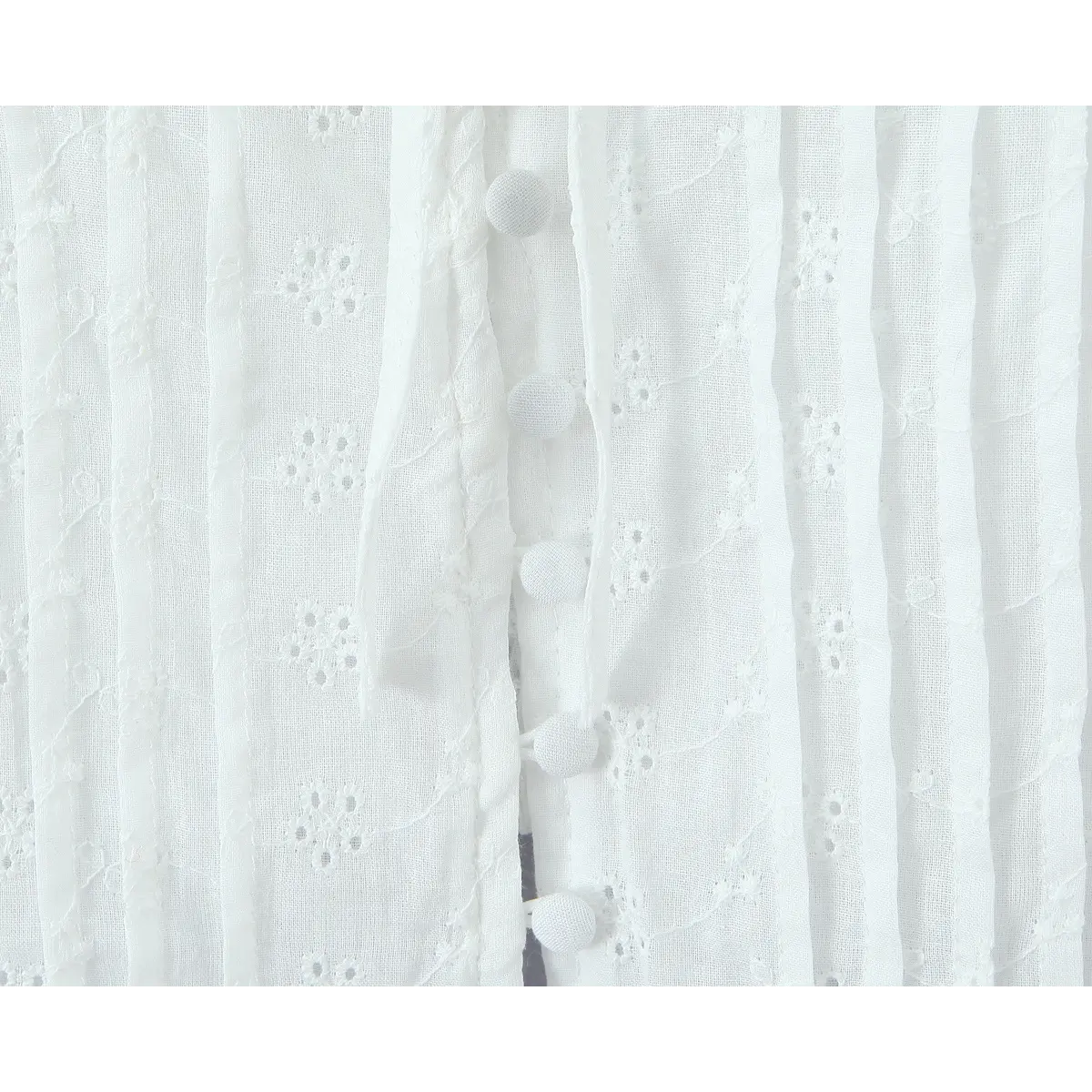 Close-up of the front button placket on a white eyelet bustier top, highlighting the fabric-covered buttons and textured pintuck details.